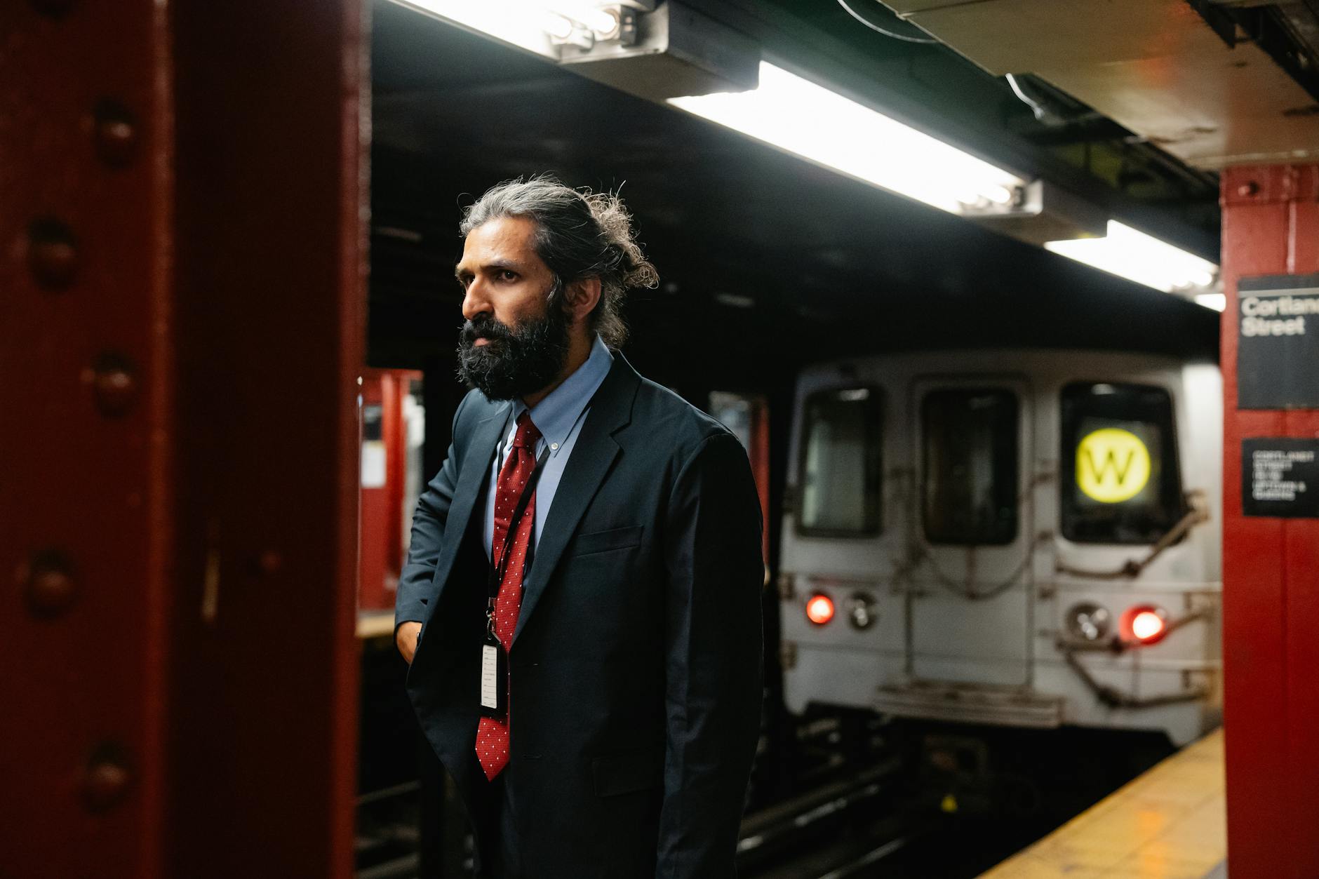 A professional man in formal attire waiting for a subway train at Cortlandt Street station.